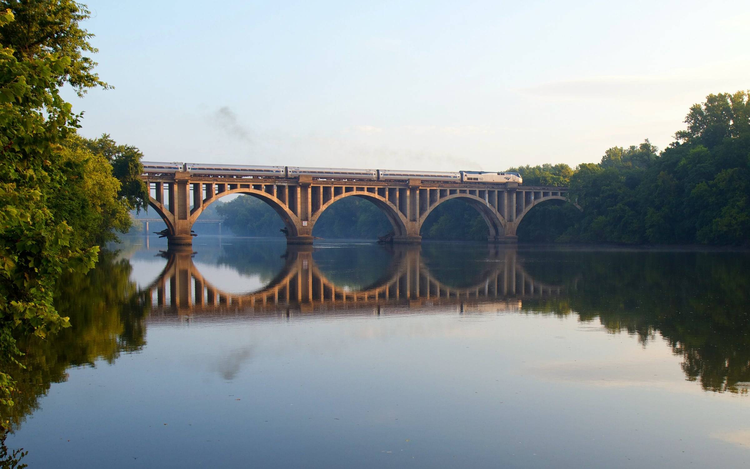 An Amtrak train crossing the arched railroad bridge over the calm Rappahannock River at Fredericksburg
